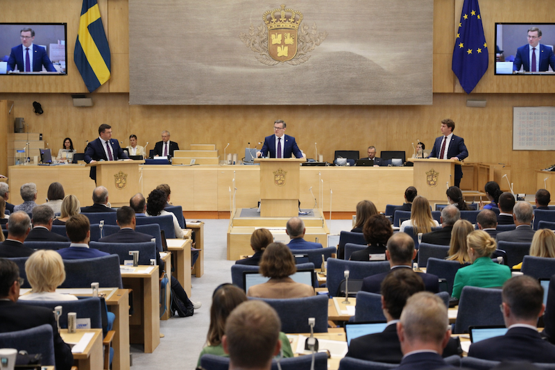 Svensk riksdag och politisk debatt – illustration av riksdagssal med talarstol, svenska flaggor och politiker i diskussion, symboliserar demokratisk beslutsprocess.